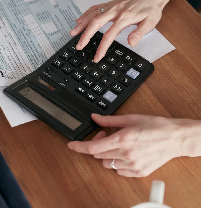 our-journey-01 Person calculating finances with a calculator and document on a wooden desk.