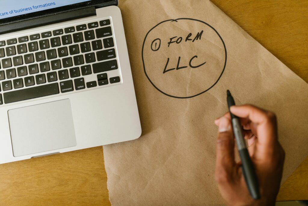 pexels photo 7310136 7310136 Close-up of hand writing 'Form LLC' on craft paper beside a laptop, indicating business planning.