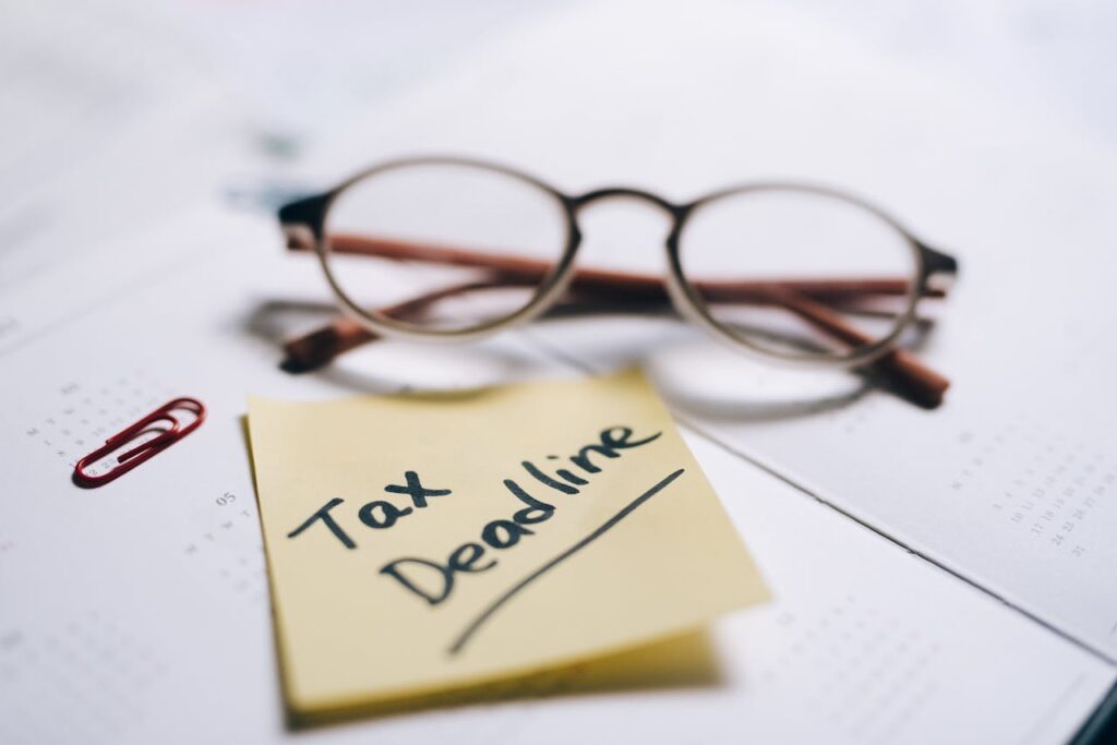 A close-up shot of a sticky note with 'Tax Deadline' written on it, alongside eyeglasses and a calendar.